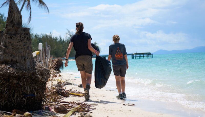 Travellers collecting plastic waste on a beach.