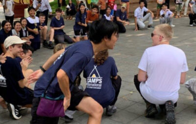 Group of students on a Camps International expedition to Cambodia playing duck duck goose with a group of Cambodian locals and school children.