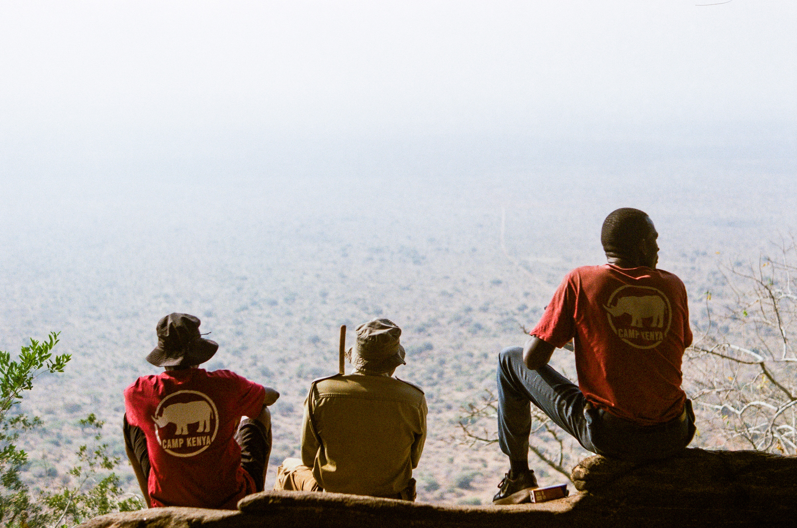 Three locals from Kenya sat on a cliff looking out into the misty horizon