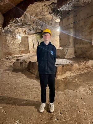 a young boy wearing yellow helmet and black clothes standing in a lit cave