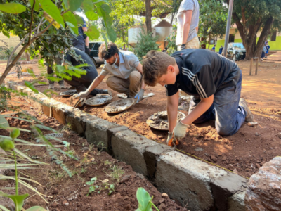 Student travellers, kneeling down on the ground working on laying foundations of a structure in Tanzania