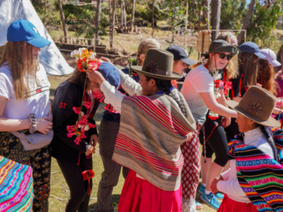 Local women in Peru wearing traditional colourful clothing putting a garland of flowers on student travellers