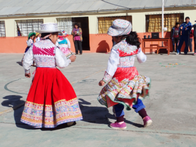 Two Peruvian children dancing together in cultural dress during break time at a local school