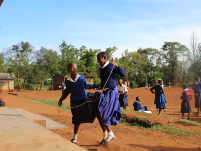 African school children playing with a skipping rope at breaktime. They're both jumping and smiling together