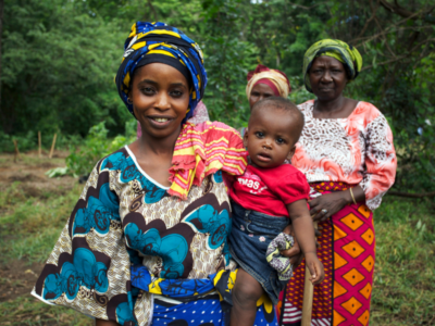 Two African Mamas in their traditional dress holding their babies on their hips