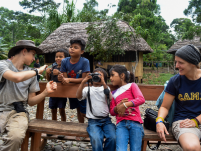 Photograph of students on an expedition with Camps International, sitting with some local children playing with cameras and taking photos